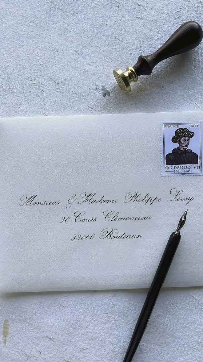 A hand-addressed envelope with a postage stamp, a dip pen and a wooden sealing-wax stamp on white paper
