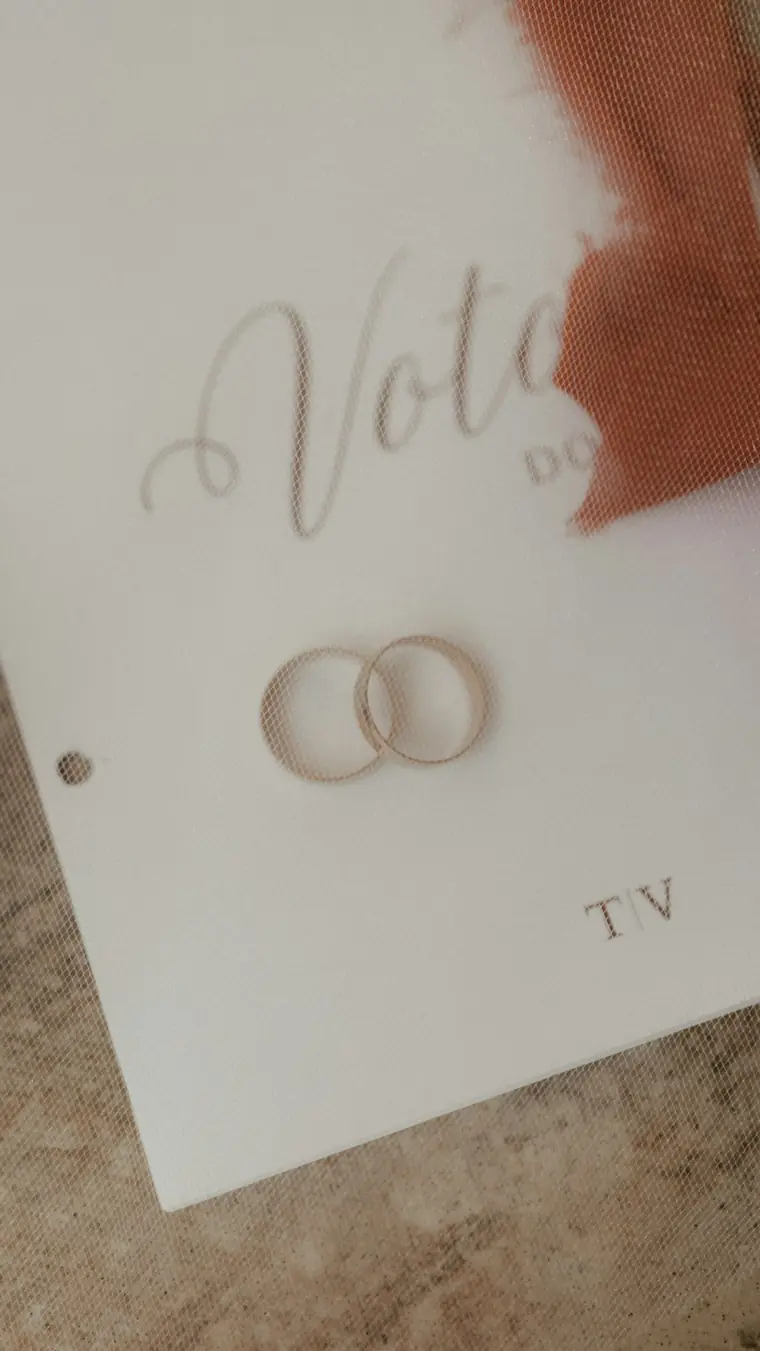 Two gold wedding rings resting on a cream vows card with a torn terracotta ribbon