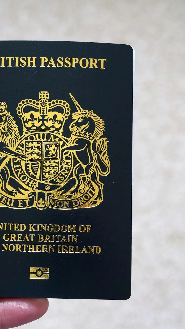 A hand holding a navy British passport with its gold royal crest