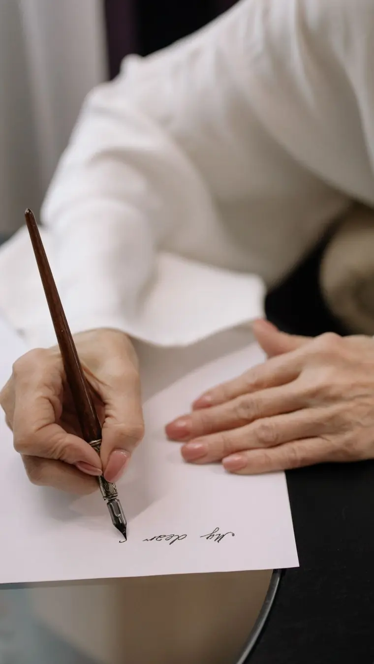 Hands writing with a slim fountain pen on a white sheet of paper
